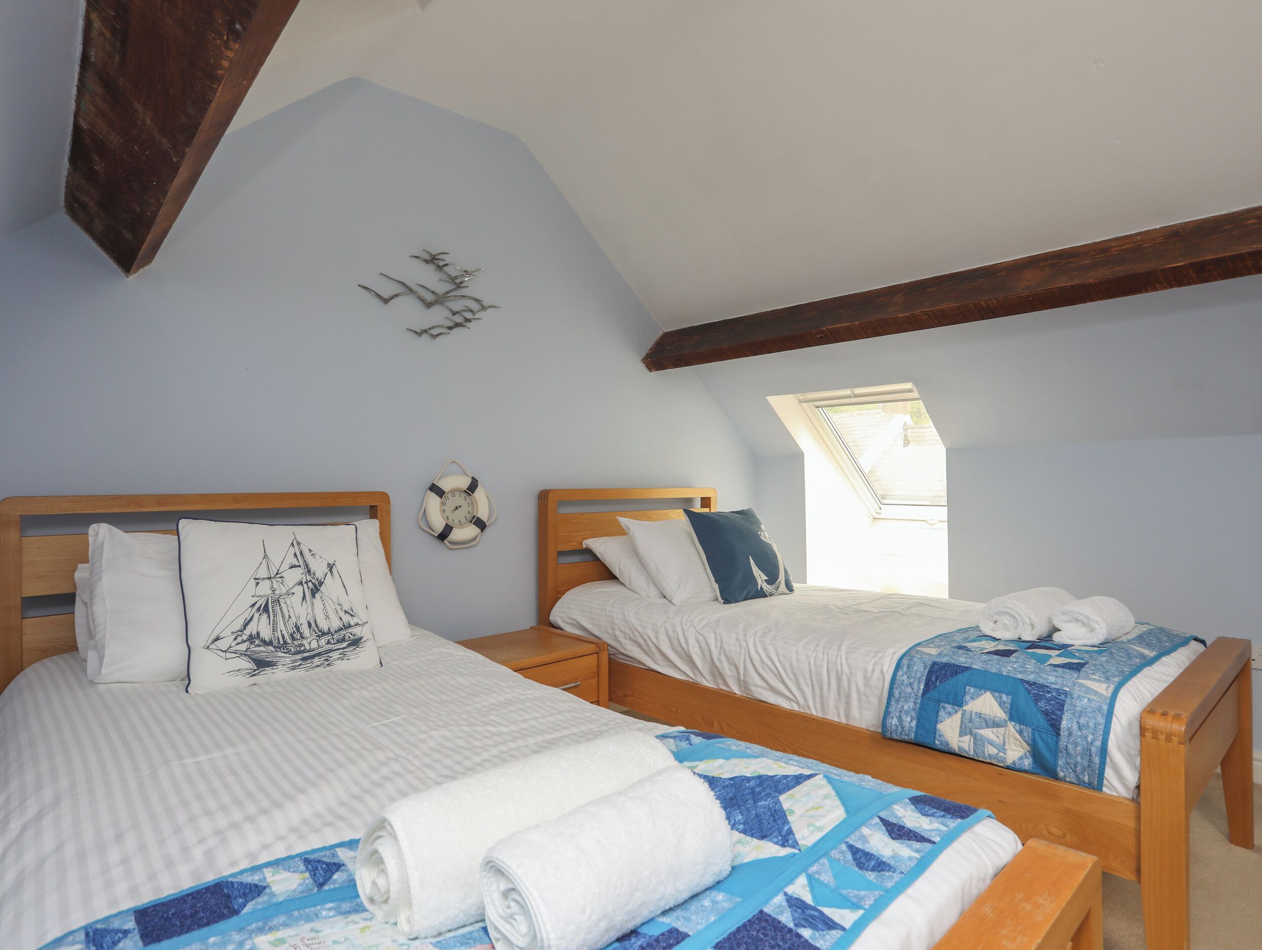 Une chambre avec deux lits, une tête de lit en bois, une petite fenêtre et une horloge murale.