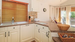 A kitchen with white cabinets, a granite countertop, a sink, and a wooden bowl on the counter. - Harvester Lodge (Weston-super-Mare)