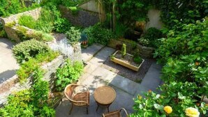Ein Garten mit einer Sitzgelegenheit, Steinmauern und verschiedenen Pflanzen.