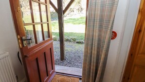 Una porta de fusta amb un panell de vidre, un estri de porta amb un dibuix de cor, i vista a una zona enjardinada.