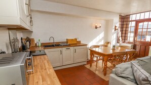 Cuina compacta amb taulell de fusta, armaris blancs, un rentapeus i una zona menjador amb taula i cadires.