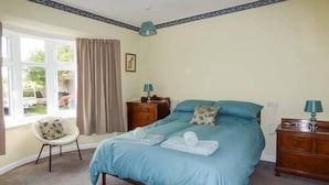 A bedroom with a bed, a chair, a dresser, and a window with curtains. - Glenhaven (Saxmundham)