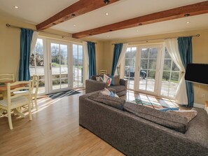 A spacious living room with a large sofa, a dining table with chairs, and a television mounted on the wall. - Erica's 'eaven (York)
