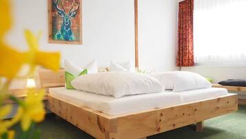 A wooden bed with white bedding, a green pillow, and a painting on the wall.