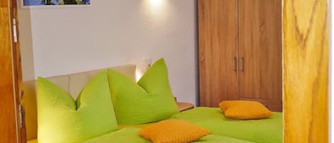 A bed with green and orange pillows, a wooden wardrobe, and a wall-mounted picture.