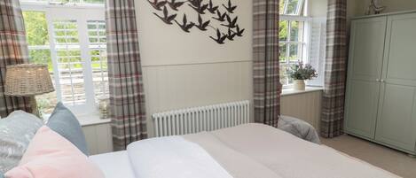 A bedroom with a bed, a radiator, a window with curtains, a wall-mounted bird decoration, a lamp, and a wardrobe.