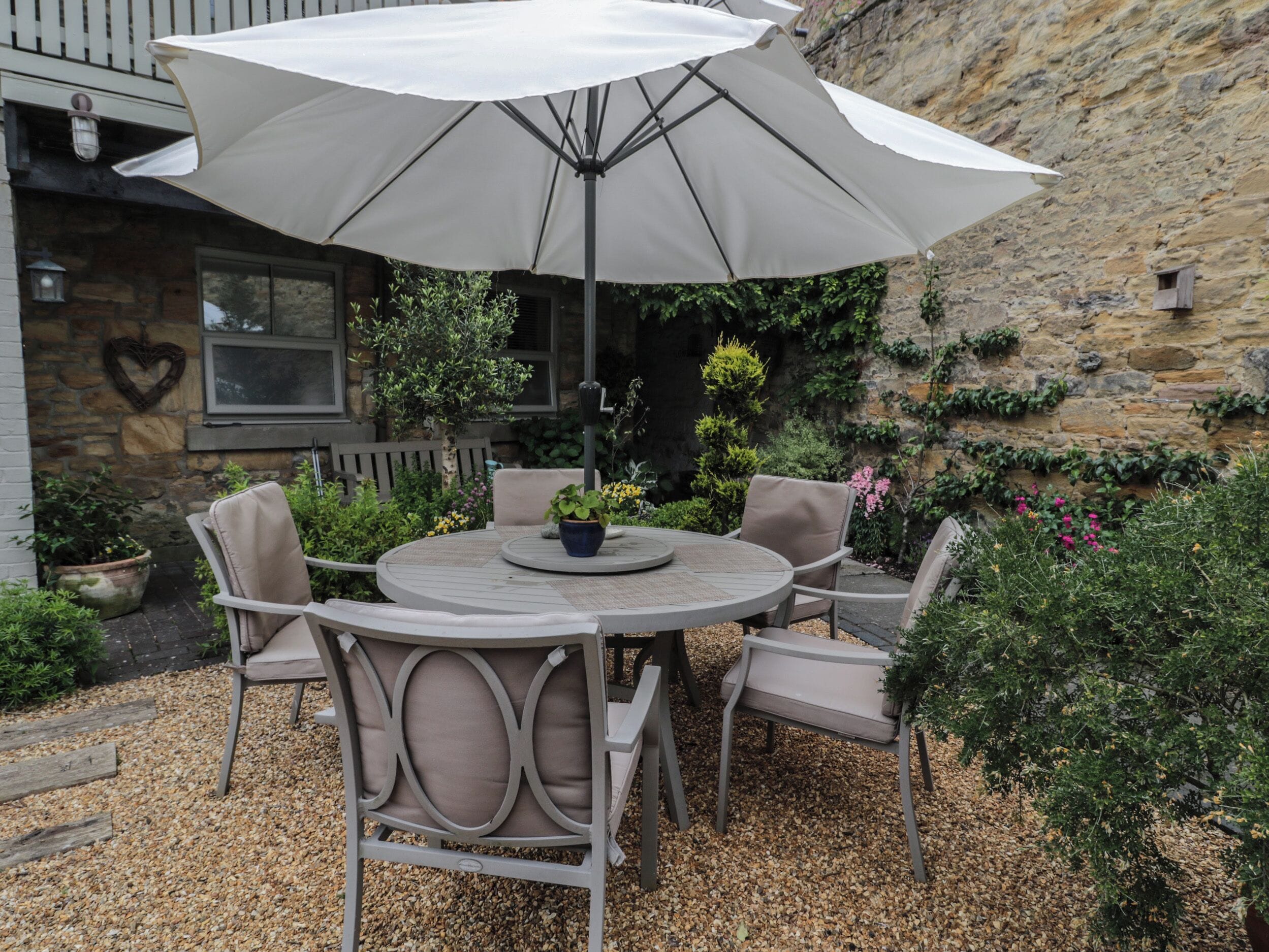 Een buitenpatio met een ronde tafel, vier stoelen en een grote parasol.