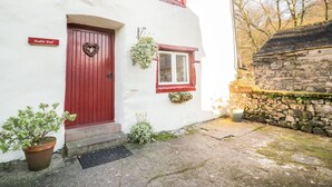 A white building with a red door, a small window with a red frame, and a stone wall to the right. - Stable End Cottage (Seascale)