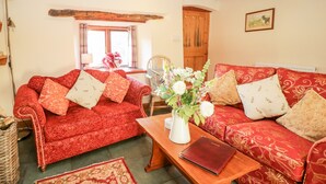 A cozy living room with a red patterned sofa, a wooden coffee table, and a vase of flowers. - Stable End Cottage (Seascale)