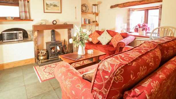 A cozy living room with a fireplace, a sofa, a table, and a bookshelf. - Stable End Cottage (Seascale)