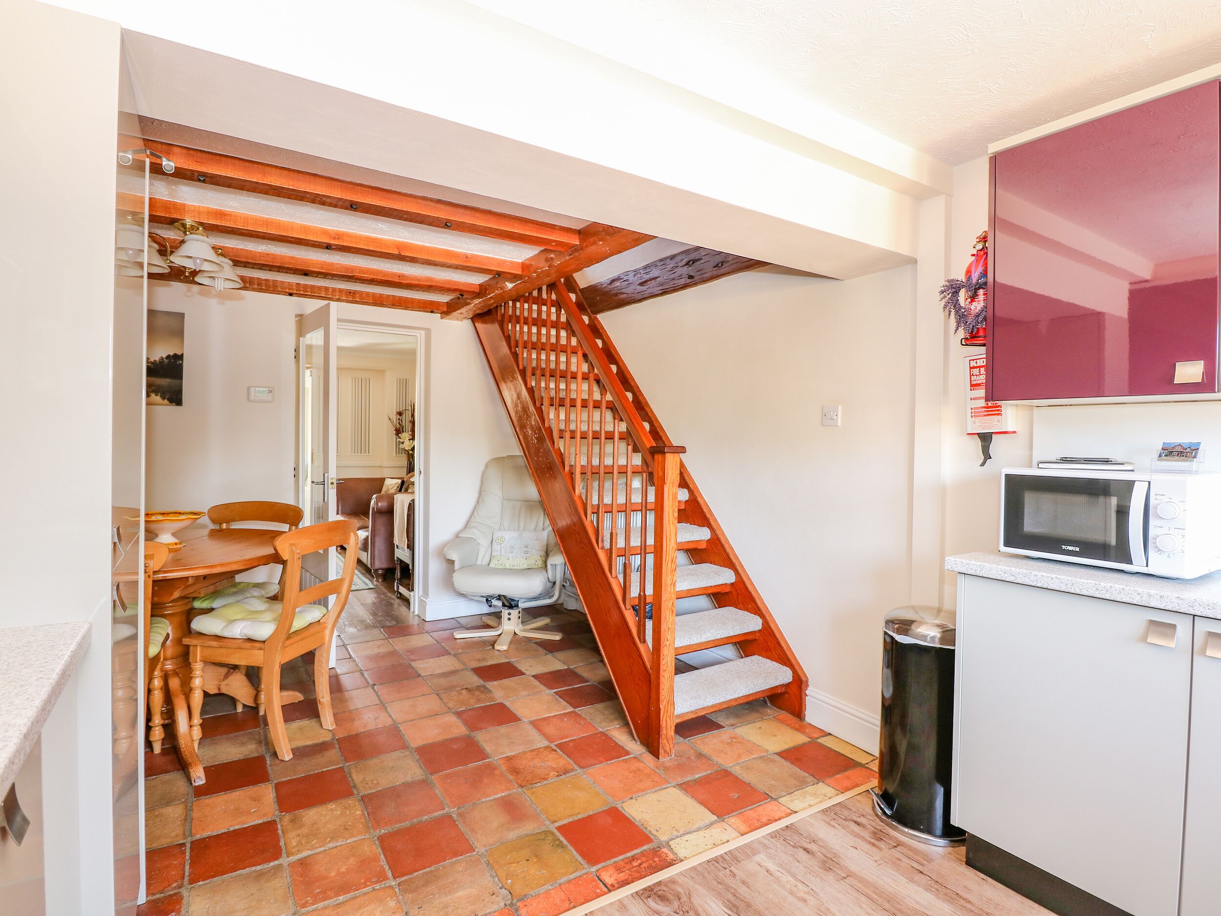 Una cocina con una escalera de madera, una zona de comedor con una mesa y sillas, y un microondas en la encimera.