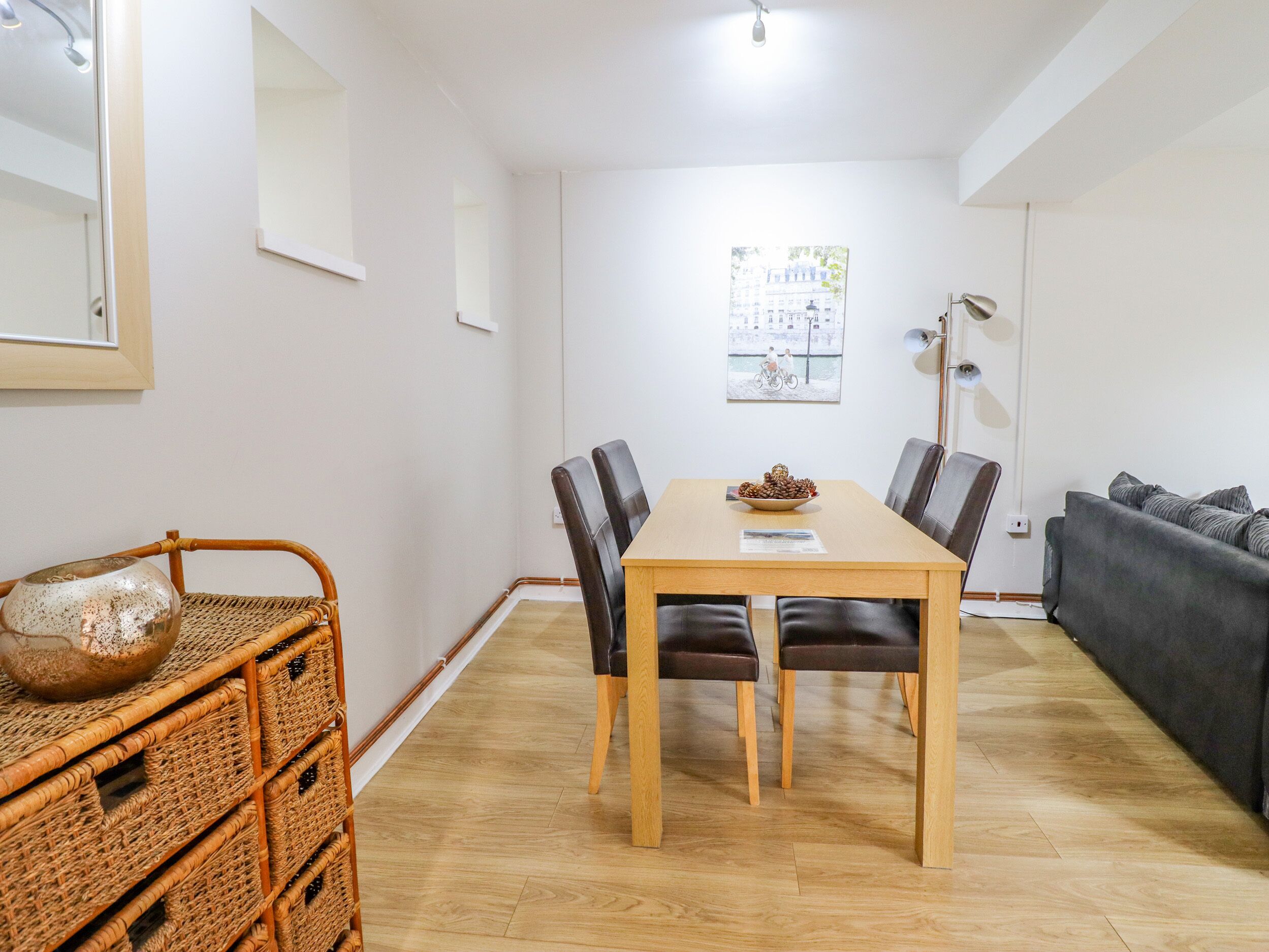A dining area with a wooden table and chairs, a wicker basket, and a gray sofa.