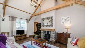 Un salon chaleureux avec une cheminée, des poutres en bois, un téléviseur et un canapé.