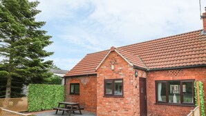 Une maison en briques avec un toit en tuiles, une clôture en bois et une table de pique-nique dans la cour.