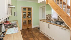 Une cuisine avec des meubles de rangement en bois, une cuisinière encastrée, un évier et un escalier menant à un palier.