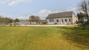 Un bâtiment en pierre avec un toit en pente, de grandes fenêtres et une cour gazonnée.