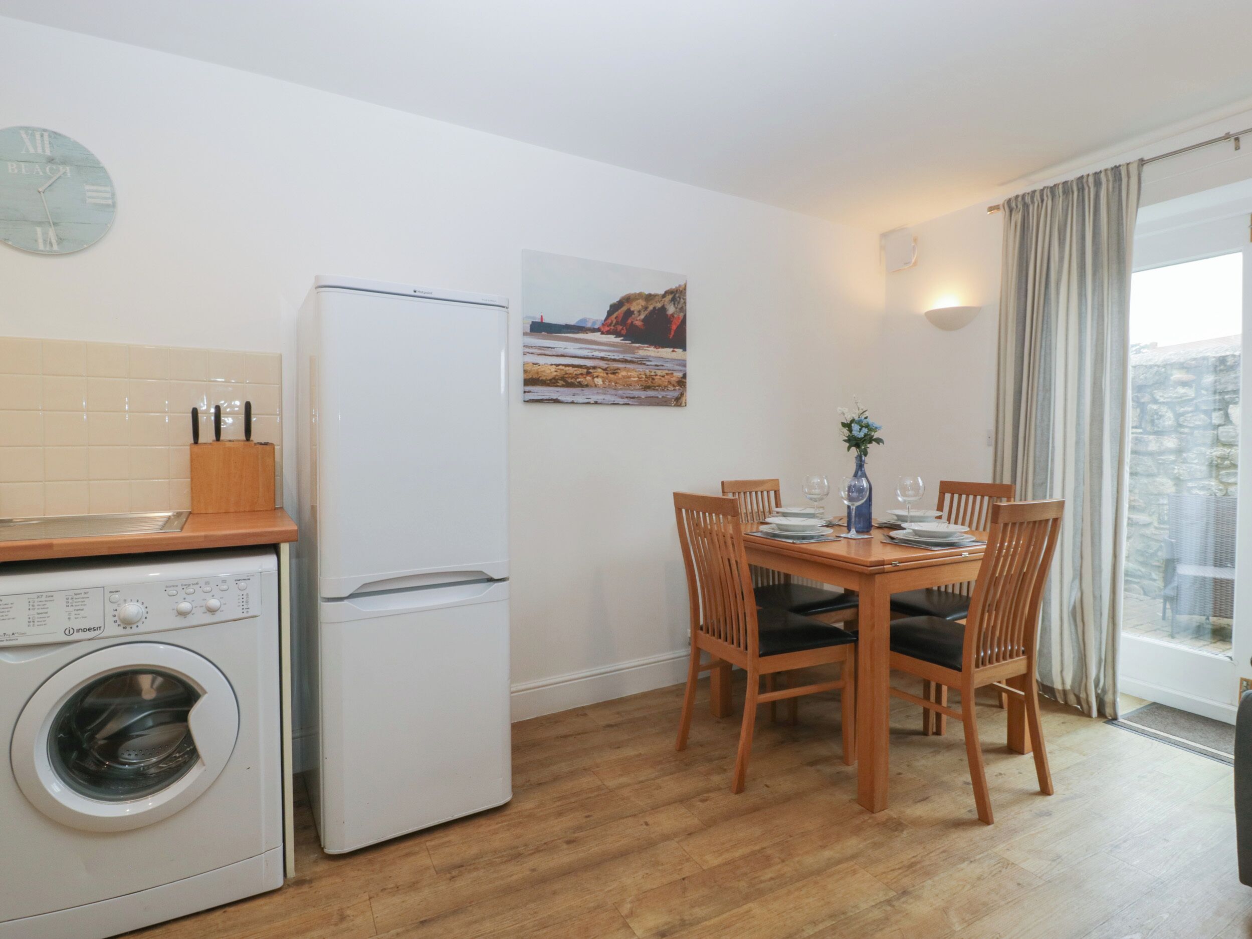 Une cuisine compacte équipée d’un lave-linge, d’un réfrigérateur, d’une table à manger avec des chaises et d’un tableau accroché au mur.
