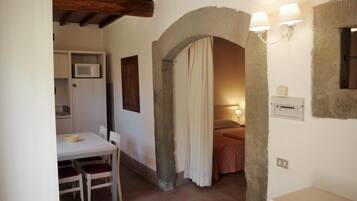 Ein Zimmer mit Esstisch, Stühlen, einer Mikrowelle, einem Bett mit Vorhang und einer Wandleuchte.
