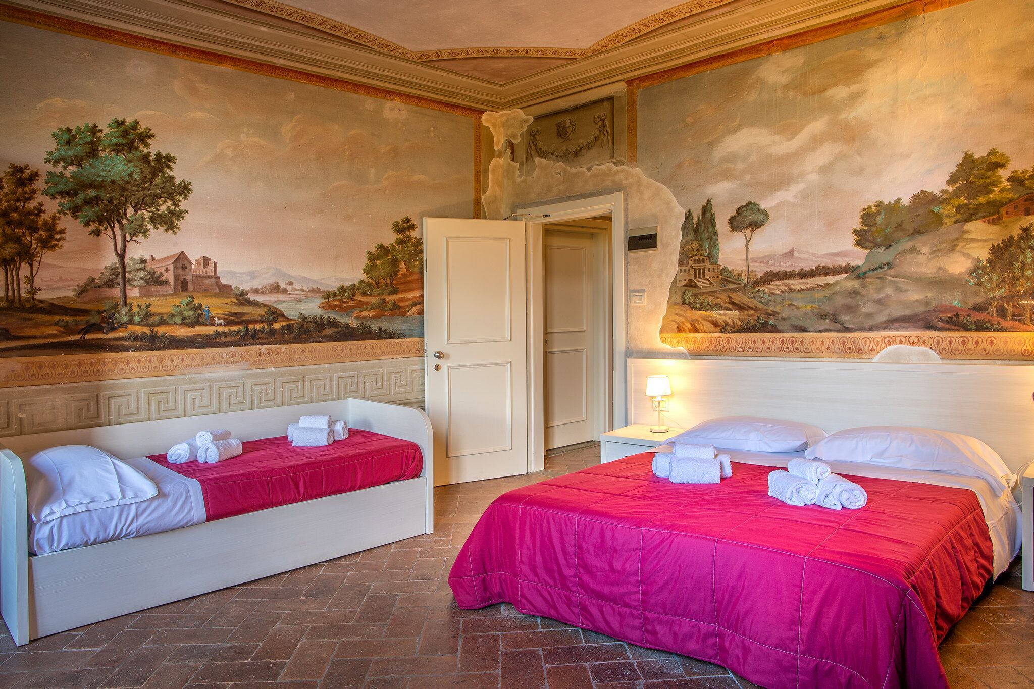 A hotel room with two beds, a mural on the wall, and a door leading to another room.