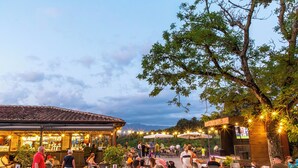 Un espacio exterior para comer con mesas y sillas, una barra y un escenario para espectáculos.