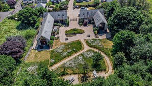 An aerial view of a residential property with two main buildings, a driveway, and surrounding greenery. - Shepherd Oak (Weymouth)