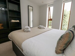Een slaapkamer met een bed, een grote spiegel, een kledingkast en een raam met uitzicht op groen.