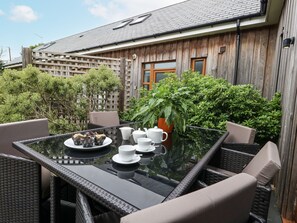Een terras buiten met een glazen tafel, rieten stoelen en een bloempot.