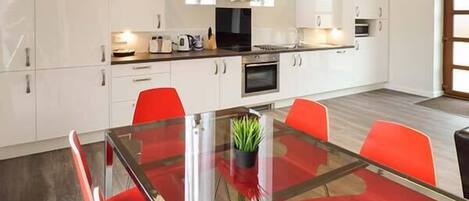 Una cocina moderna con armarios blancos, una mesa de comedor de vidrio con sillas rojas y un horno empotrado.