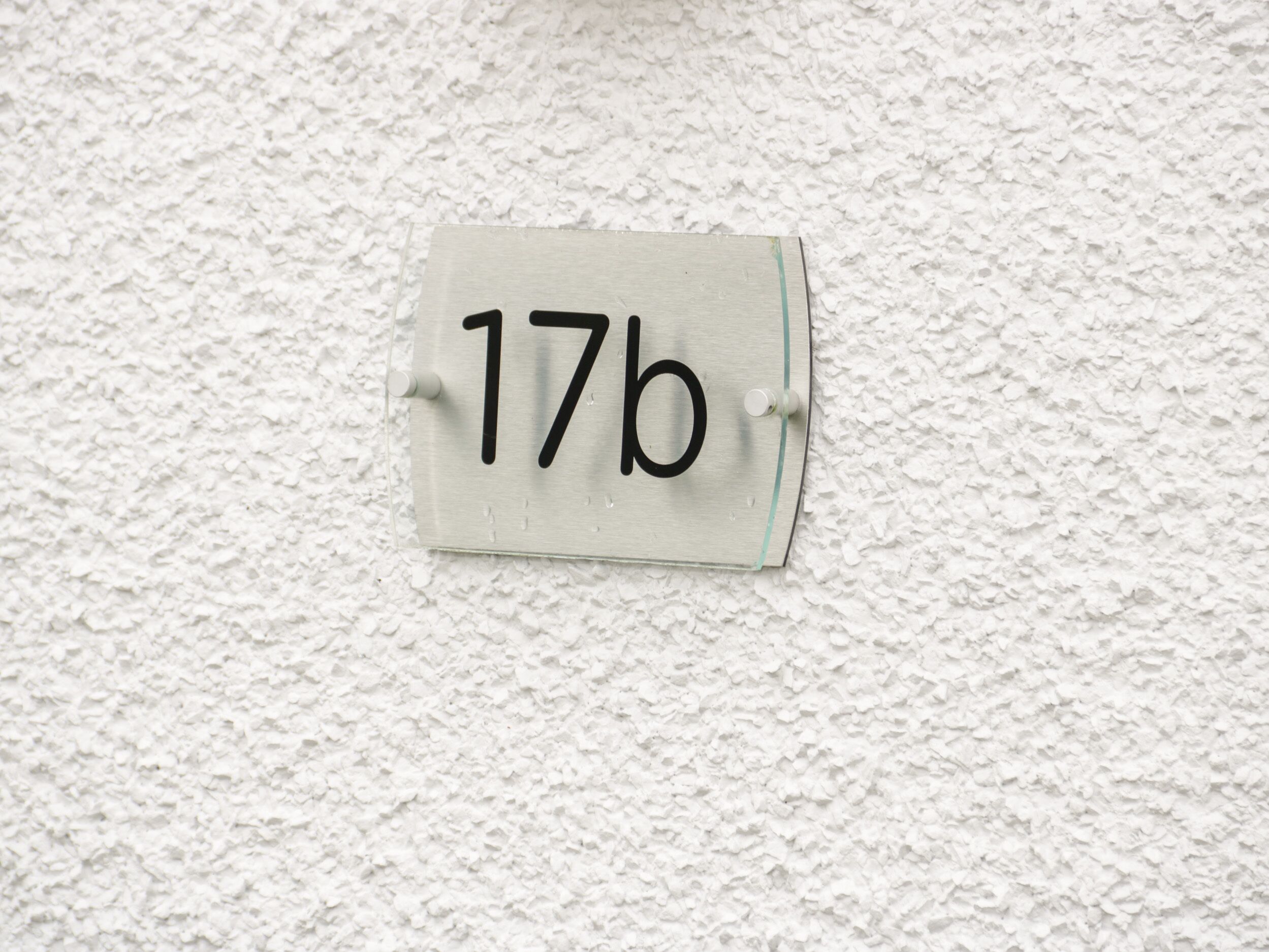 Un panneau indiquant le numéro de la maison, « 17b », fixé à un mur blanc à texture.