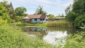 A house with a large glass window, a pond in front, and a garden with various plants. - Dragonfly Lodge (Dereham)