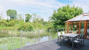 A deck with a table and chairs overlooking a pond with lily pads. - Dragonfly Lodge (Dereham)