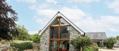 A modern house with a stone exterior, large glass windows, and a patio with outdoor furniture.