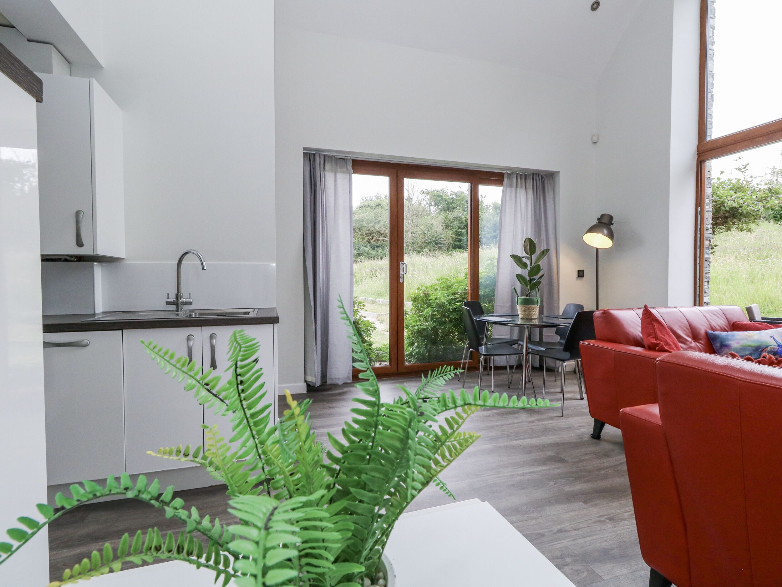 A modern kitchen with a sink and cabinets, a dining area with a table and chairs, and a red sofa.