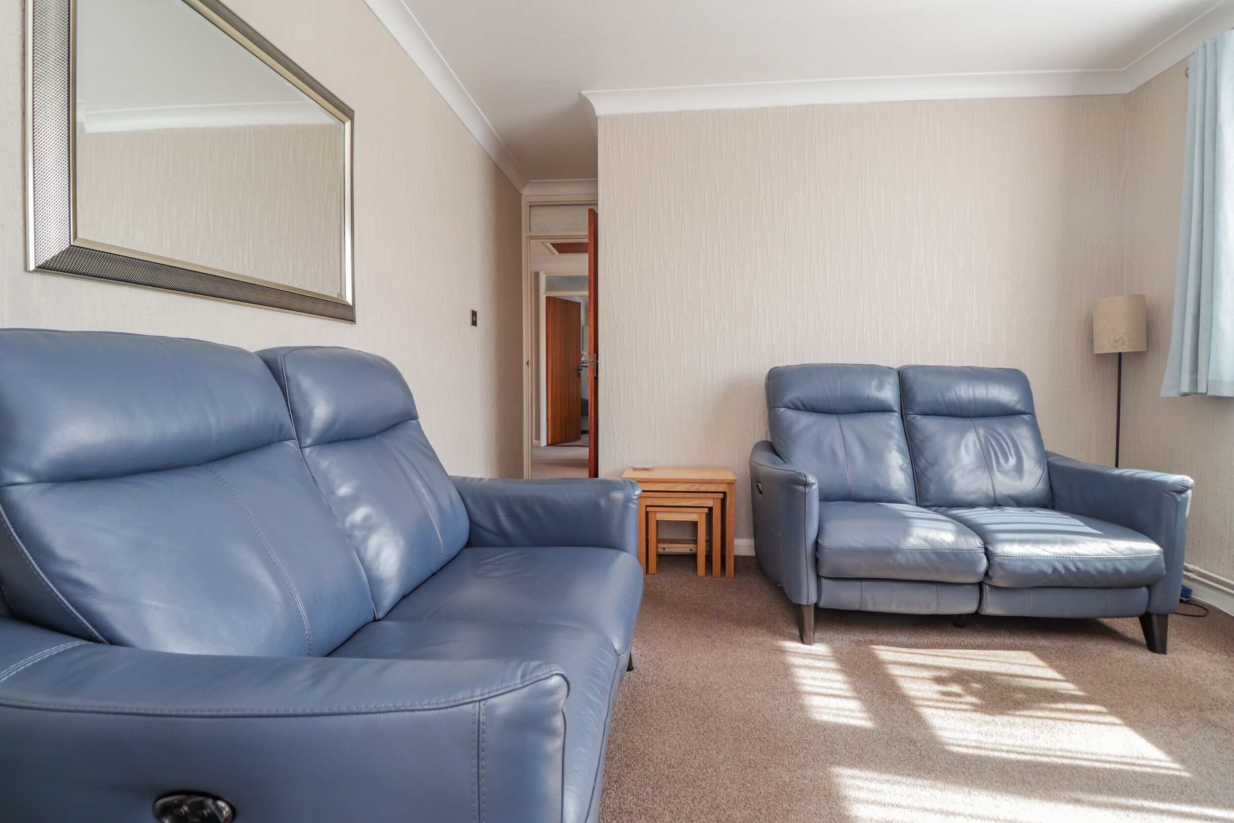 A room with a blue leather sofa, a matching armchair, a small wooden table, and a lamp.