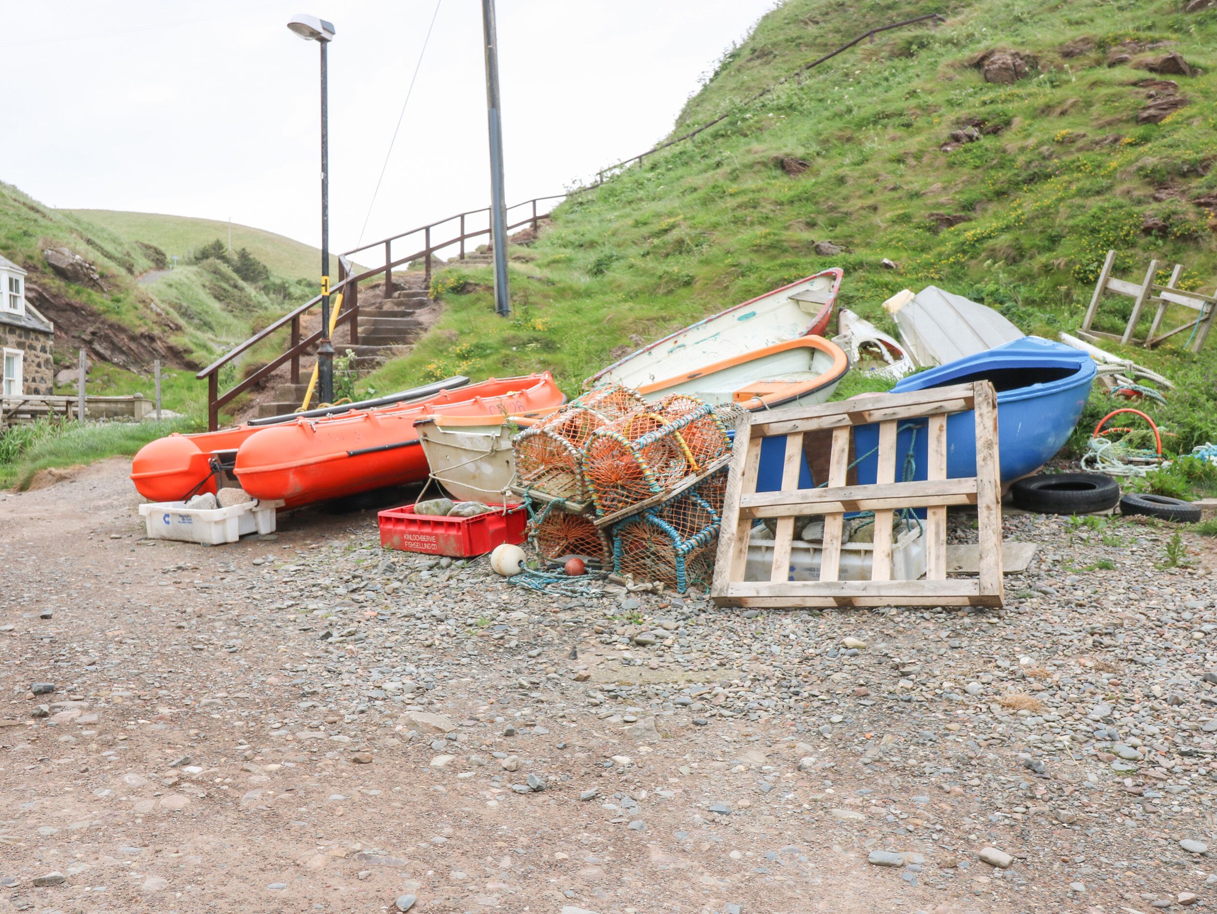 A gravel path leading to a staircase with boats and fishing gear piled up.