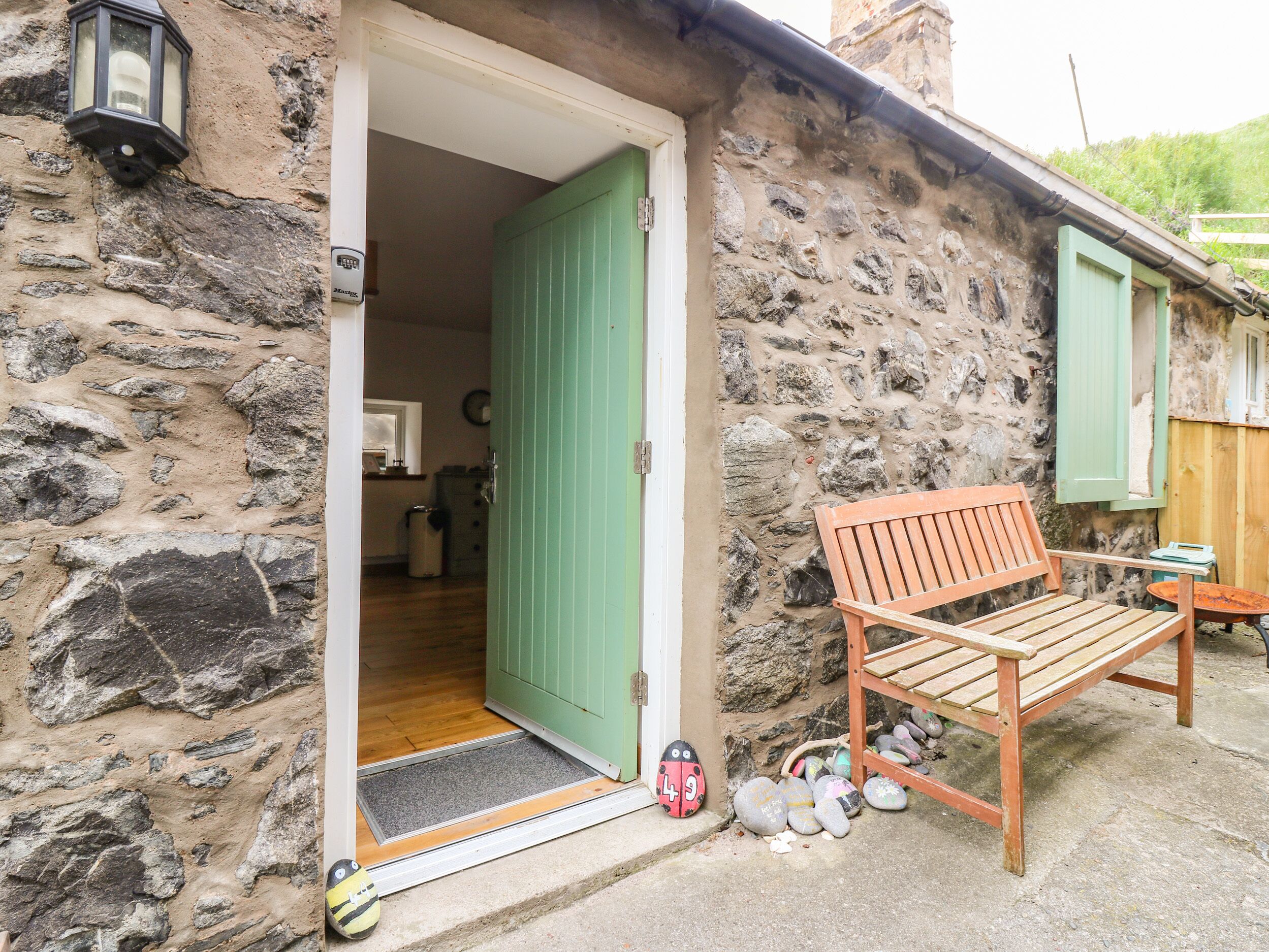 A stone building with a green door, a wooden bench, and a doormat with a ladybug design.