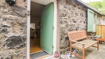 A stone building with a green door, a wooden bench, and a doormat with a ladybug design.