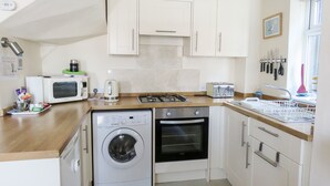 A compact kitchen with a washing machine, microwave, toaster, and a gas stove. - Odd Sock Cottage (Whitby)