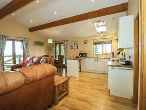 A spacious living area with a leather sofa, wooden flooring, and a dining area with a table and chairs. - Valley View Lodge (Welshpool)