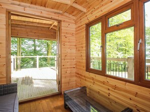 A wooden cabin with a sliding glass door leading to an outdoor deck, a glass table, and a bench.