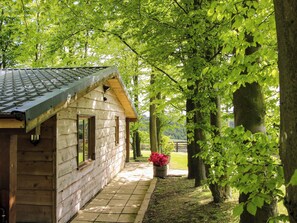 A wooden cabin with a tiled roof, a stone pathway, and a large tree with green leaves. - Valley View Lodge (Welshpool)