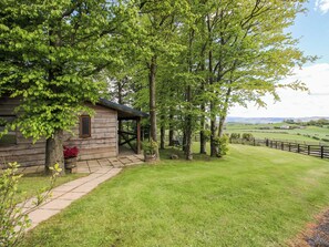 A wooden cabin with a porch, surrounded by lush greenery and a view of rolling hills.