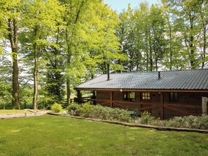 A wooden cabin with a tiled roof, surrounded by lush greenery and trees. - Valley View Lodge (Welshpool)