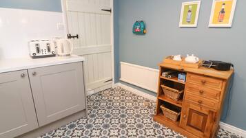 Cocina compacta con armarios blancos, piso estampado, mueble de madera con cestas y cuadros en la pared.