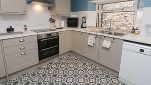 A modern kitchen with a built-in oven, a dishwasher, and a window with a stone wall view. - 9 Tower Street (Richmond)