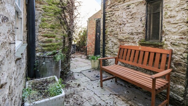 A narrow alley with a wooden bench, stone walls, and potted plants. - 9 Tower Street (Richmond)