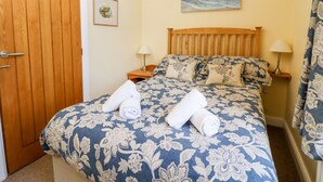 Un dormitorio con una cama de madera, ropa de cama floral, dos lámparas de noche, un cuadro en la pared y una puerta.