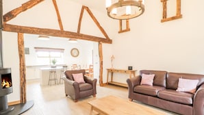 Una sala de estar acogedora con chimenea, un sofá de cuero marrón, una mesa de centro de madera y una estructura de techo rústica de madera.