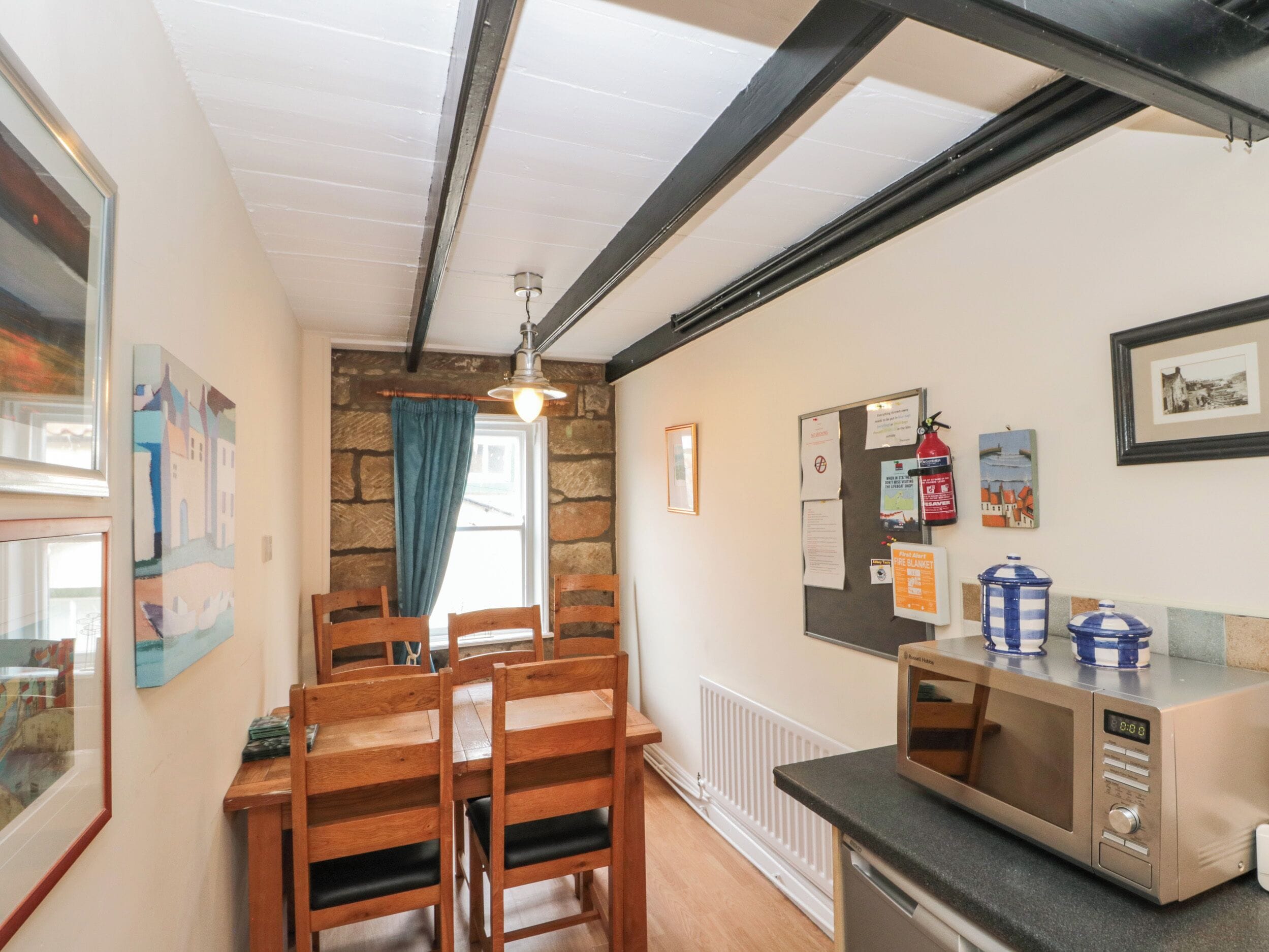 A compact kitchen with a wooden dining table, chairs, a microwave, and a refrigerator.