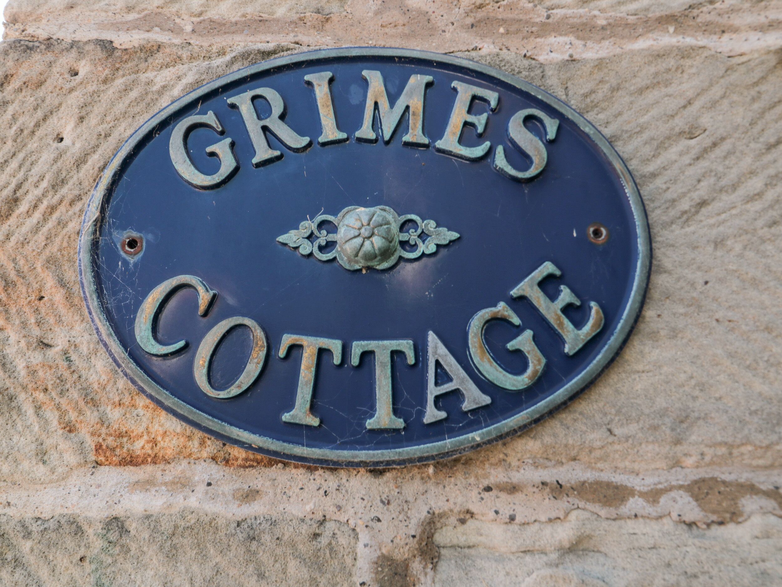 A blue metal sign with the words "GRIMES COTTAGE" on a stone wall.